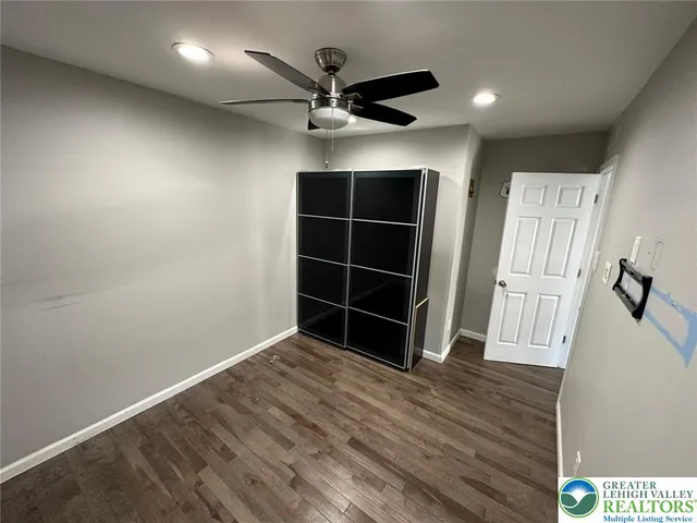 a view of an empty room with wooden floor and a ceiling fan