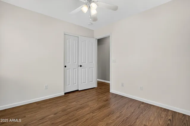 a view of an empty room with wooden floor and fan