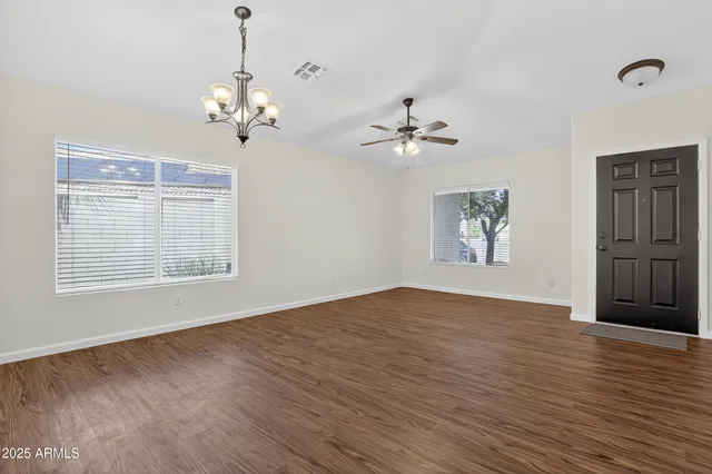 an empty room with wooden floor chandelier fan and windows
