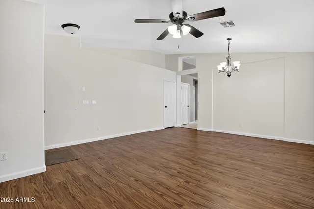 an empty room with wooden floor chandelier fan and windows