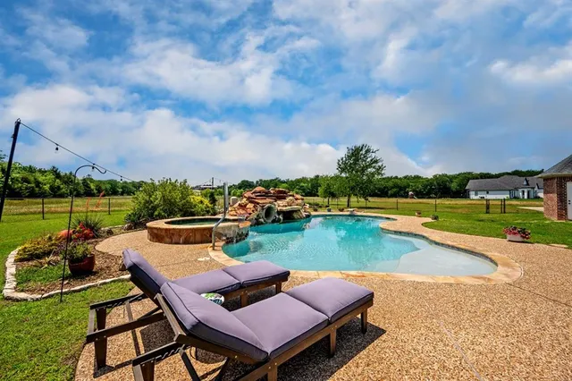 a view of a swimming pool and lounge chairs in back yard of the house