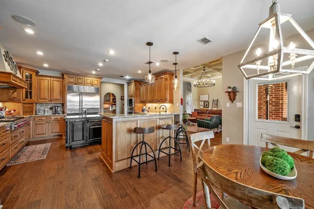 a kitchen with stainless steel appliances granite countertop a stove top oven a refrigerator a dining table and chairs with wooden floor