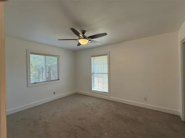 an empty room with ceiling fan and windows