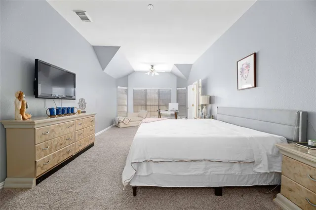 a spacious bedroom with a bed and a flat tv screen on dresser