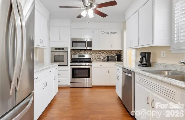 a white kitchen with stainless steel appliances granite countertop a refrigerator a stove a sink and white cabinets with wooden floor