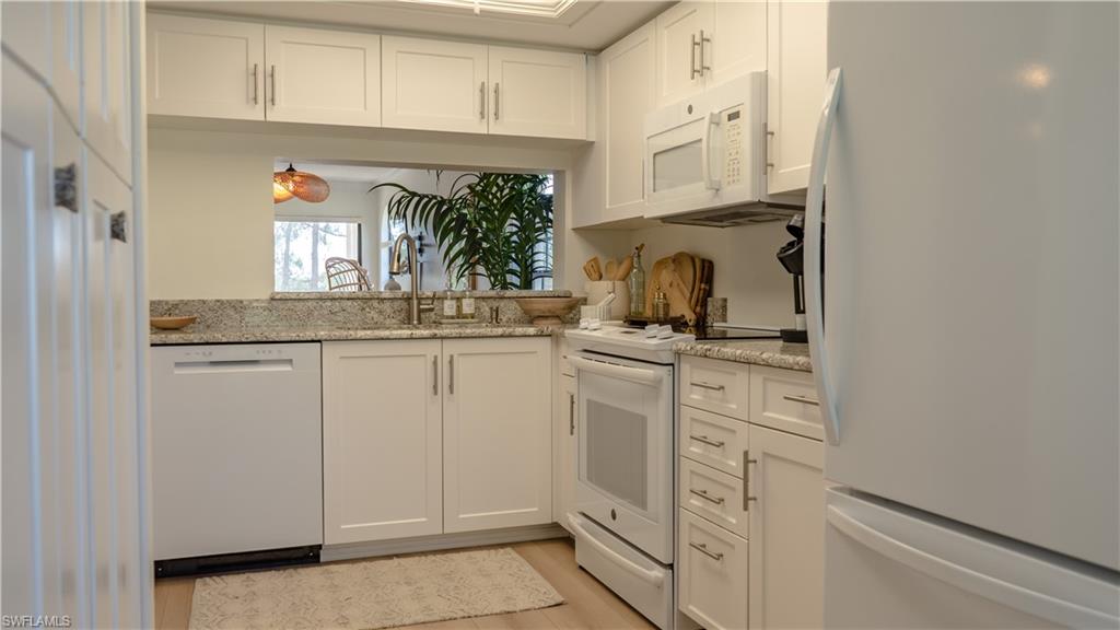 265 Deerwood Circle, Unit 10 Naples, FL 34113 - Photo 17 of 38 Kitchen with white cabinets, a sink, white appliances, light wood-style floors, and light stone countertops