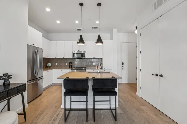 a kitchen with stainless steel appliances a dining table chairs refrigerator and microwave