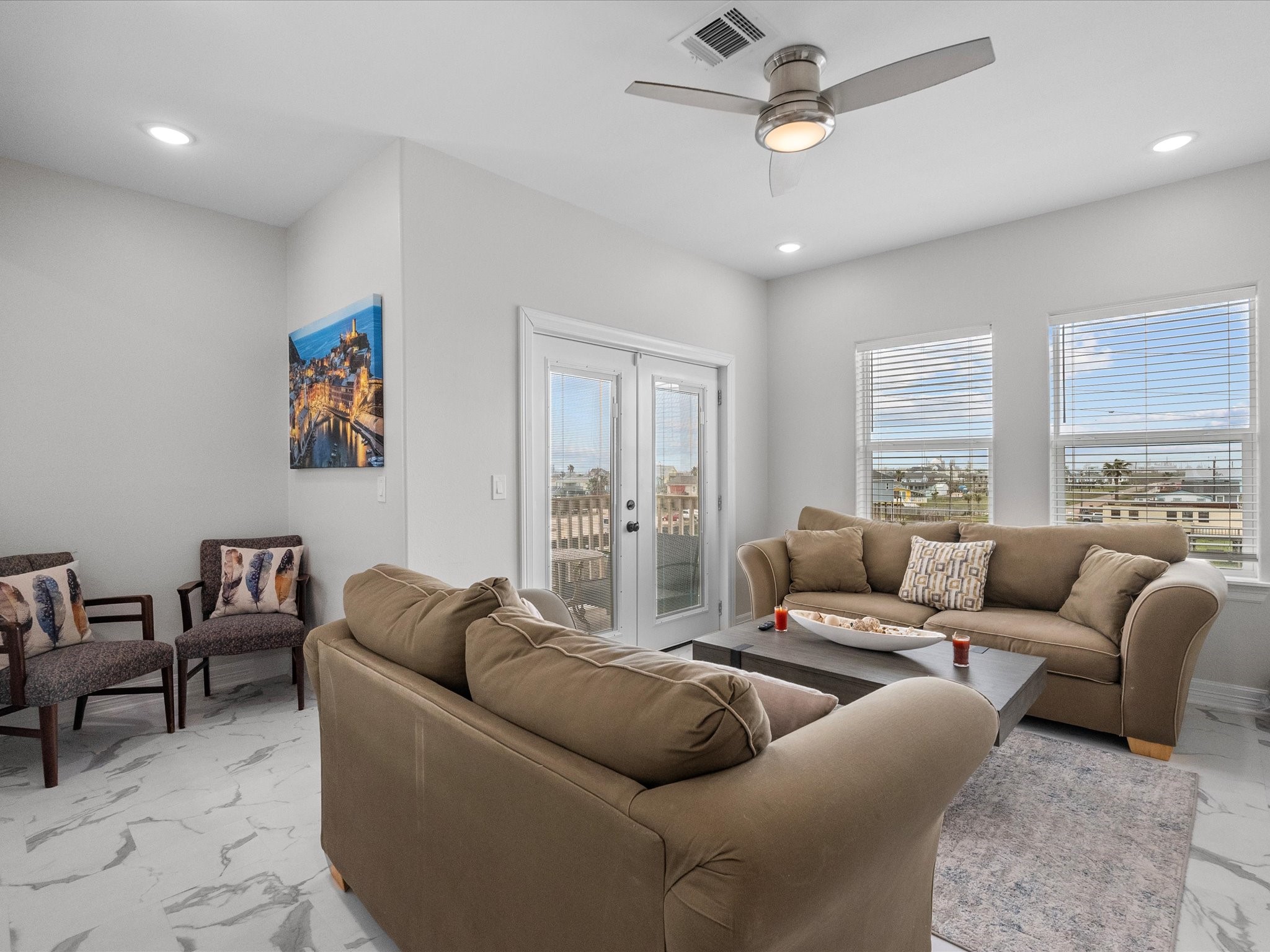1018 Seashell Drive Surfside Beach, TX 77541 - Photo 34 of 49 Bright and airy living room with modern decor, featuring comfortable sofas, a ceiling fan, and large windows offering plenty of natural light. French doors lead to an outdoor view, enhancing the spacious feel. Marble-patterned flooring adds elegance.