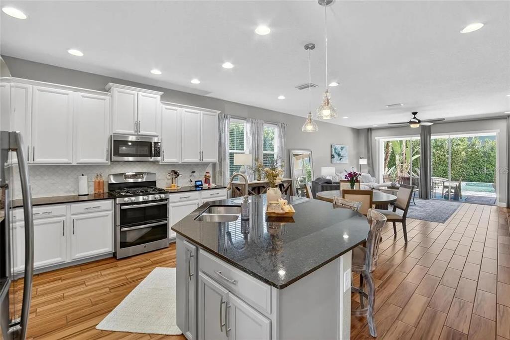 14302 Rolling Dune Road Lithia, FL 33547 - Photo 14 of 88 a kitchen with stainless steel appliances granite countertop a stove top oven a sink dishwasher a dining table and chairs with wooden floor