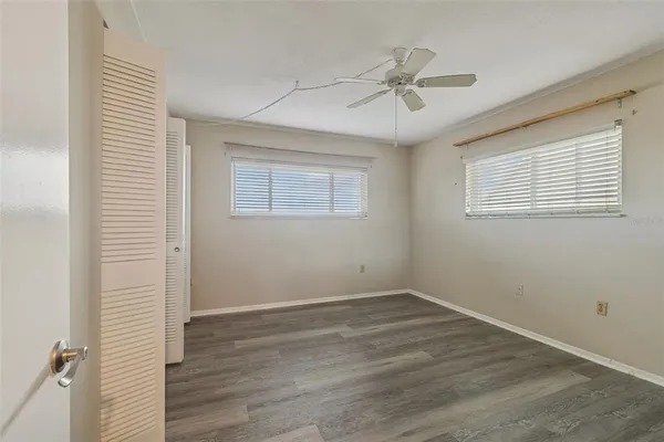 an empty room with wooden floor fan and windows