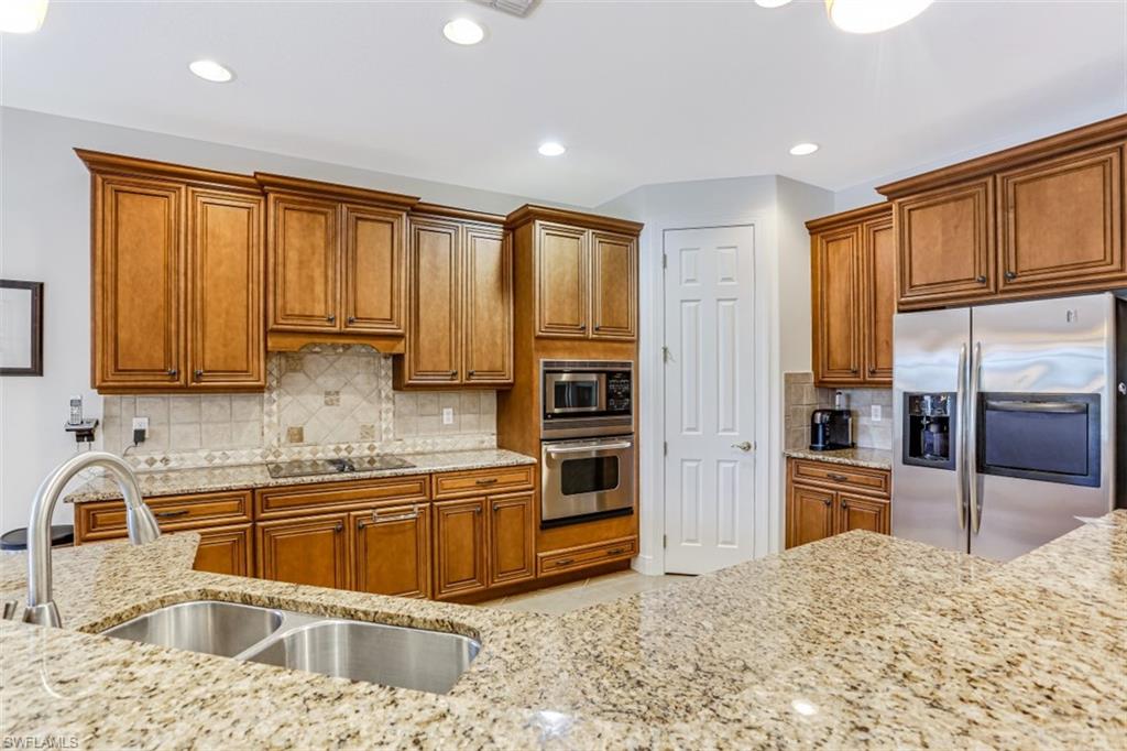 a kitchen with stainless steel appliances granite countertop a refrigerator a stove and a sink with wooden cabinets