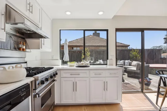 a kitchen with stainless steel appliances kitchen island granite countertop a refrigerator a stove a dining table and chairs with wooden floor