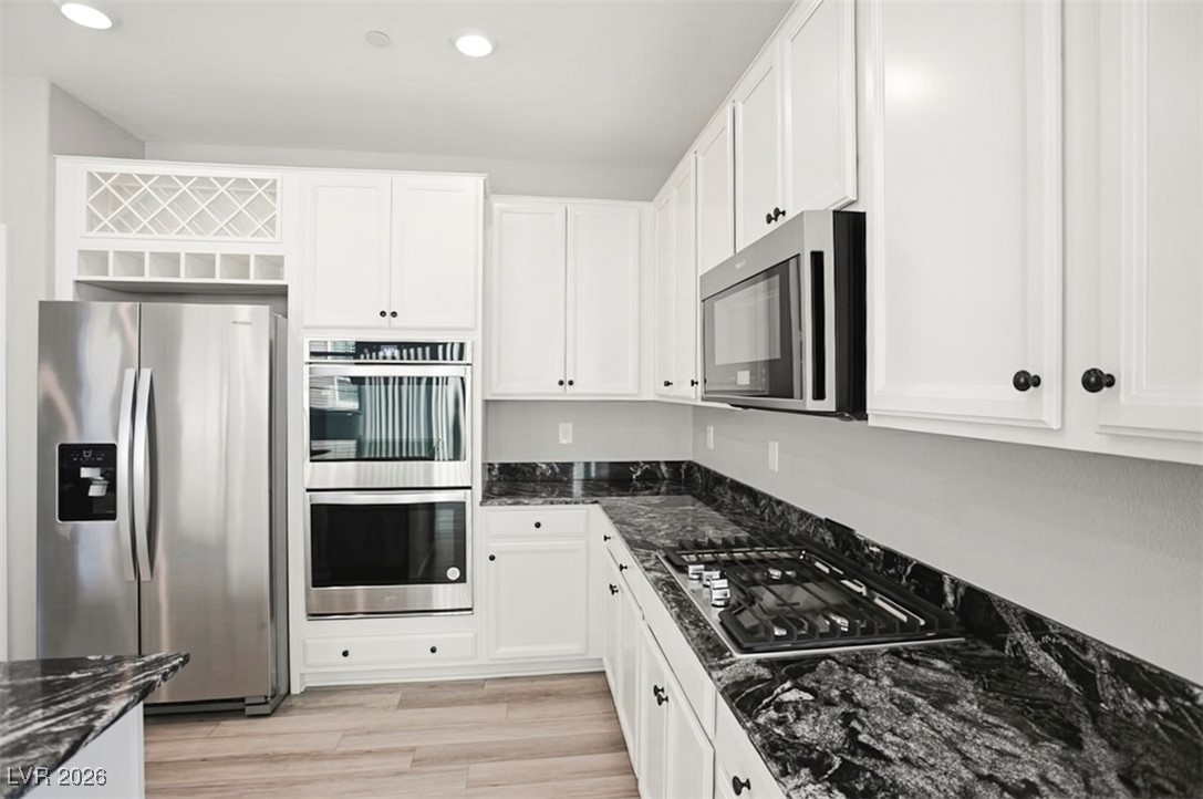 2865 Mincio Street Henderson, NV 89044 - Photo 8 of 33 Kitchen with dark stone countertops, stainless steel appliances, white cabinetry, light wood-type flooring, and recessed lighting