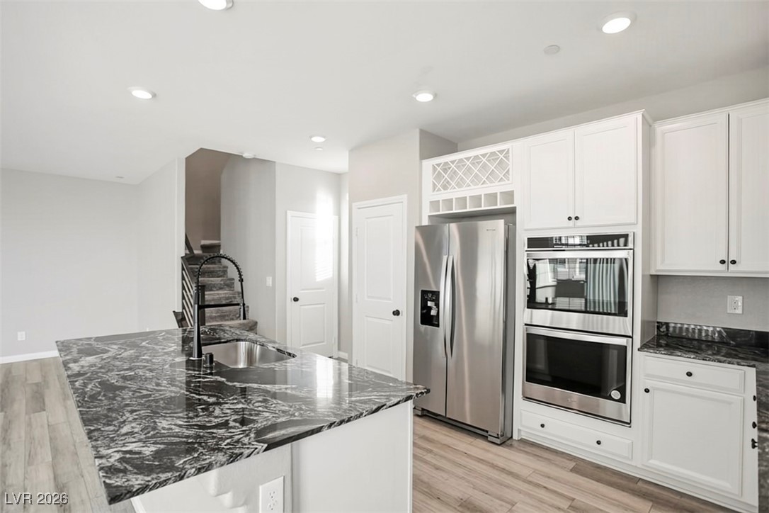 2865 Mincio Street Henderson, NV 89044 - Photo 9 of 33 Kitchen featuring dark stone countertops, appliances with stainless steel finishes, light wood-style floors, a center island with sink, and white cabinetry