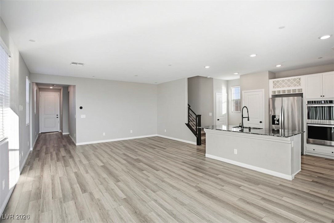 2865 Mincio Street Henderson, NV 89044 - Photo 29 of 33 Kitchen featuring white cabinetry, stainless steel appliances, open floor plan, a center island with sink, and light wood finished floors