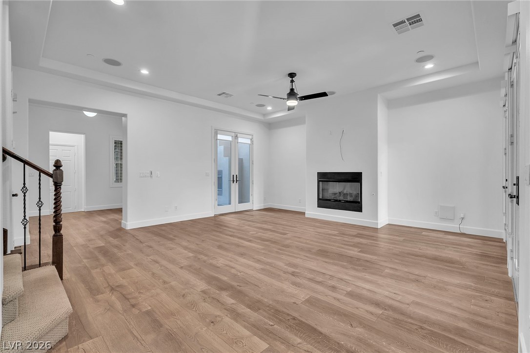11280 Granite Ridge Drive, Unit 1037 Las Vegas, NV 89135 - Photo 13 of 51 Unfurnished living room with recessed lighting, a ceiling fan, a raised ceiling, light wood-style floors, and a glass covered fireplace