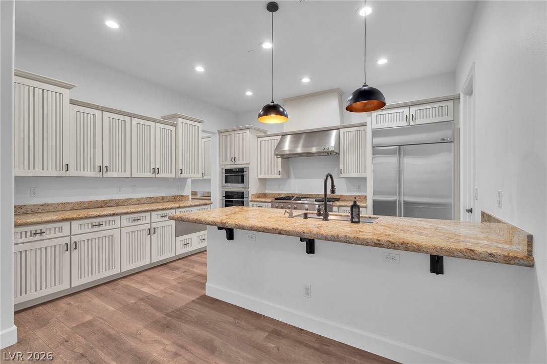 11280 Granite Ridge Drive, Unit 1037 Las Vegas, NV 89135 - Photo 21 of 51 Kitchen featuring light stone counters, a peninsula, a kitchen breakfast bar, decorative light fixtures, and light wood finished floors