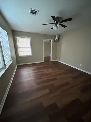 an empty room with wooden floor fan and windows