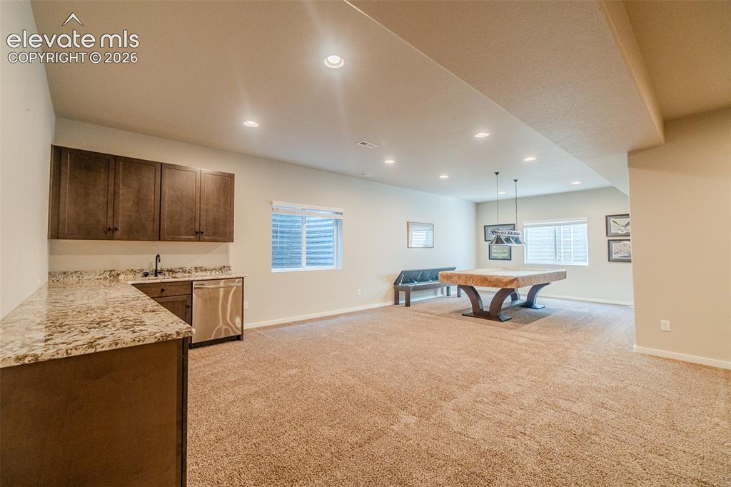 1061 Native Dancer Terrace Colorado Springs, CO 80921 - Photo 35 of 50 Entertainment room featuring recessed lighting, plush carpet flooring, a wet bar with a stainless steel sink and dishwasher, and two egress windows