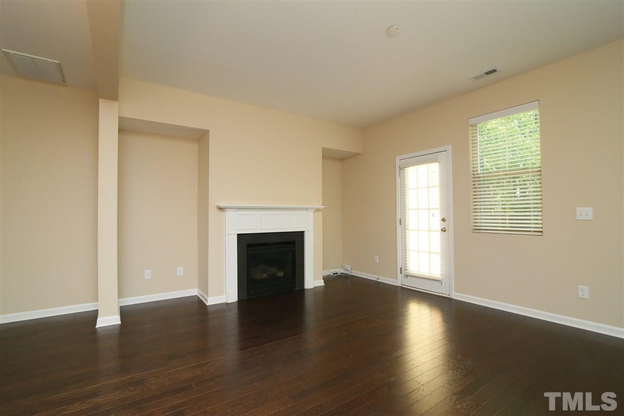 728 Wickham Ridge Road Apex, NC 27539 - Photo 4 of 21 an empty room with wooden floor fireplace and windows