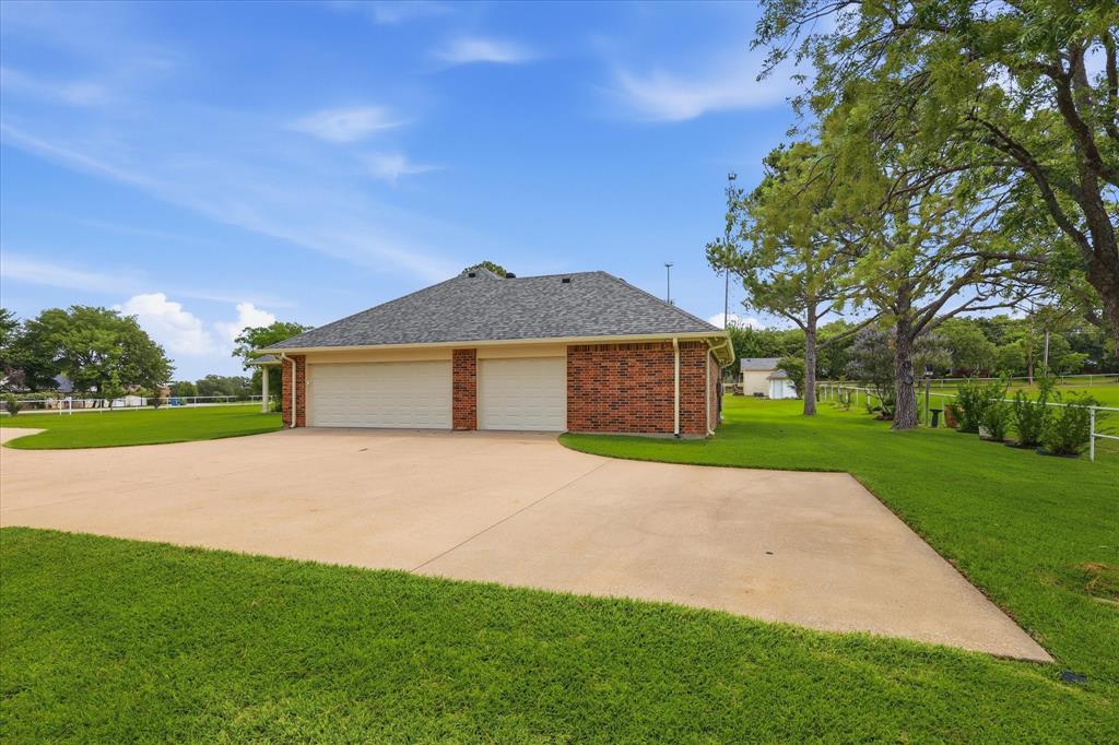 6955 Hawk Road Flower Mound, TX 75022 - Photo 3 of 40 Brick-clad garage structure featuring two overhead doors, a paved driveway, a shingled roof, and surrounding green lawn