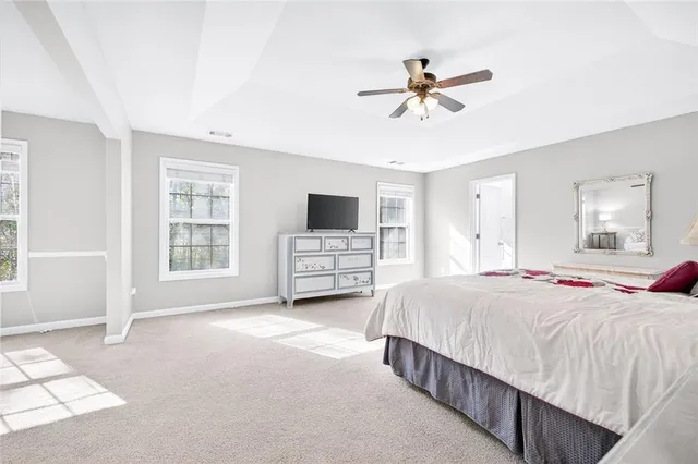 a spacious bedroom with a bed flat screen tv and windows