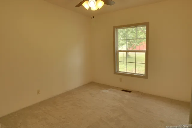 an empty room with a chandelier fan and windows