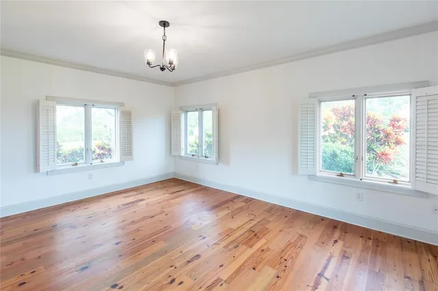 an empty room with wooden floor chandelier fan and windows