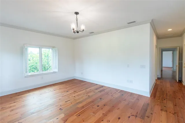 an empty room with wooden floor chandelier and windows