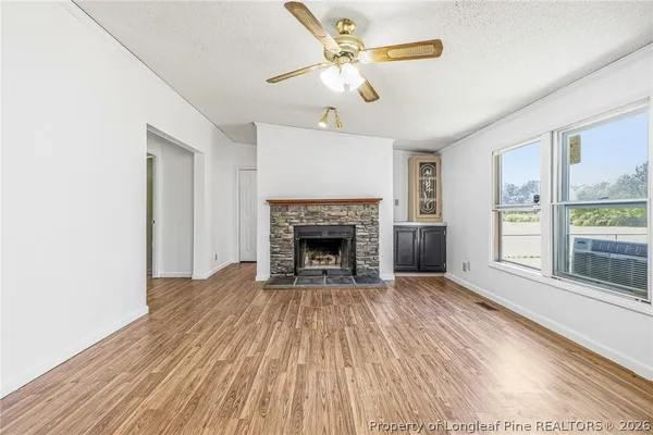 a view of a livingroom with a fireplace a ceiling fan and wooden floor
