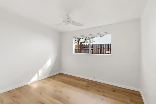 an empty room with wooden floor fan and window