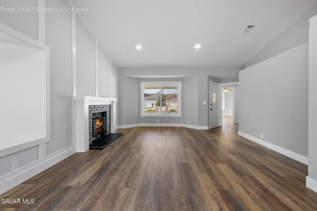 an empty room with wooden floor fireplace and windows