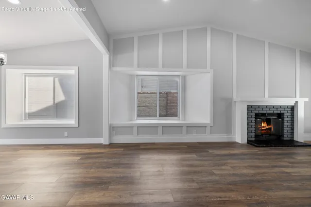 a view of an empty room with wooden floor fireplace and a window