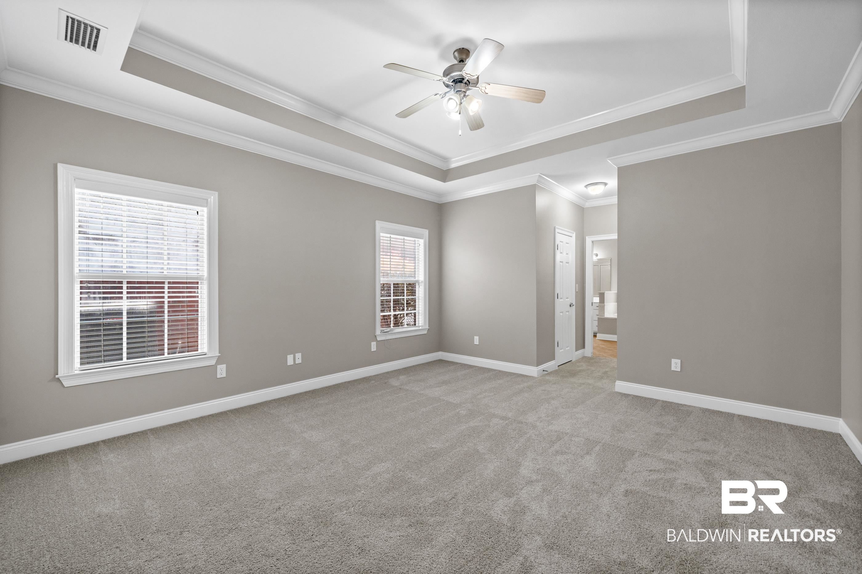 303 Savannah Circle Foley, AL 36535 - Photo 19 of 34 Spacious room featuring tray ceilings, crown molding, light gray wall paint, two windows with blinds, and light gray carpeting