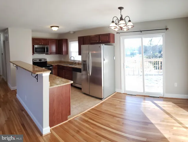 a kitchen with stainless steel appliances granite countertop a refrigerator a sink dishwasher a stove and a dining table with wooden floor