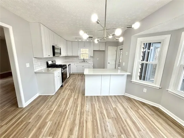 a large kitchen with stainless steel appliances kitchen island granite countertop a refrigerator a stove a sink dishwasher and white cabinets with wooden floor