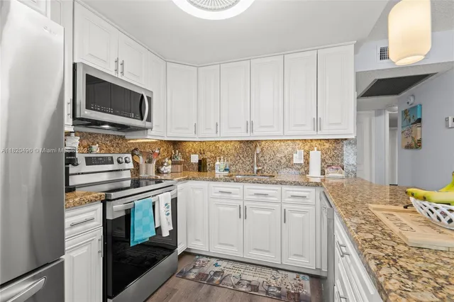 a kitchen with stainless steel appliances granite countertop a stove top oven a sink dishwasher and white cabinets with wooden floor