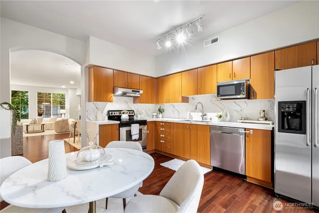 a kitchen with stainless steel appliances kitchen island granite countertop a sink dishwasher a dining table and chairs with wooden floor