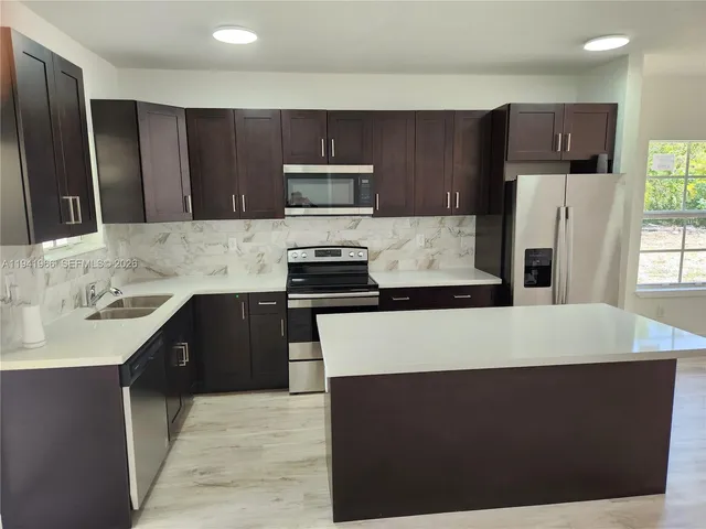 a kitchen with kitchen island granite countertop a refrigerator stove a sink and dishwasher with wooden cabinet