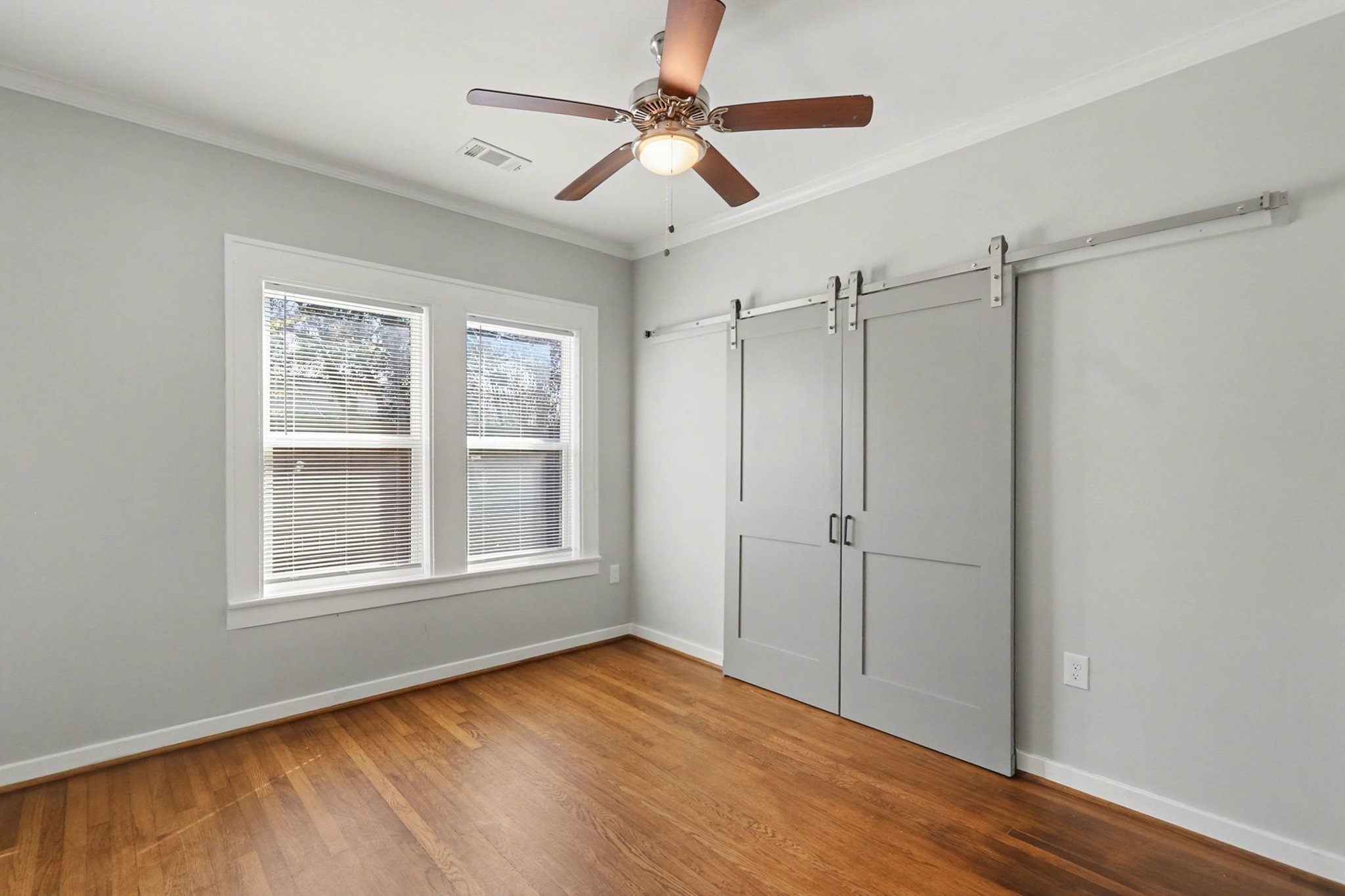 1901 Lexington Street Houston, TX 77098 - Photo 13 of 32 Discover the charm of this east-facing secondary bedroom, featuring elegant hardwood floors, crown molding, and new windows, with stylish barn doors revealing a spacious closet.