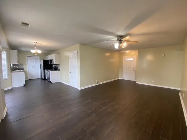 an empty room with wooden floor and a kitchen