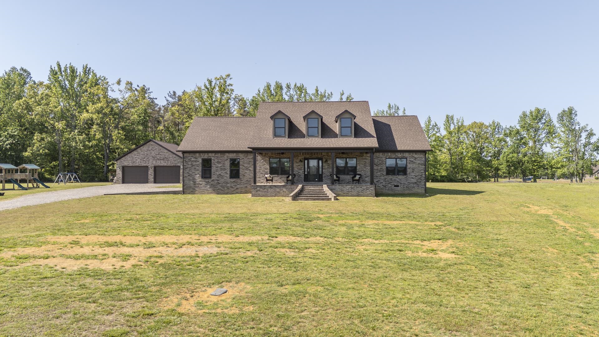 New england style home featuring a porch, a front lawn, gravel driveway, and brick siding