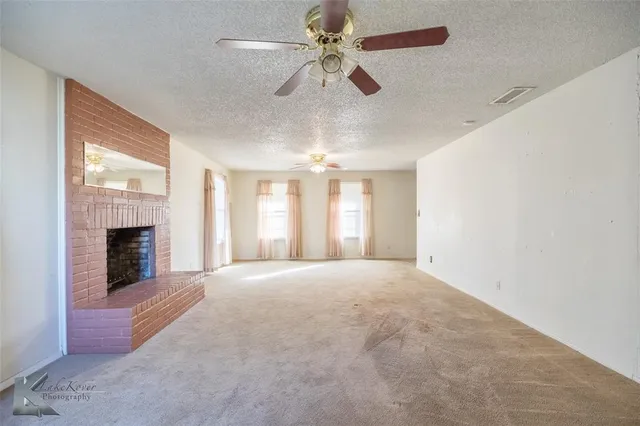 a view of an empty room with a fireplace and a chandelier fan