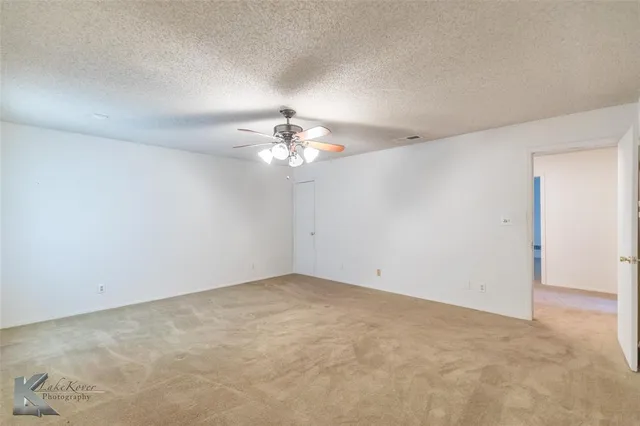 an empty room with chandelier fan and windows