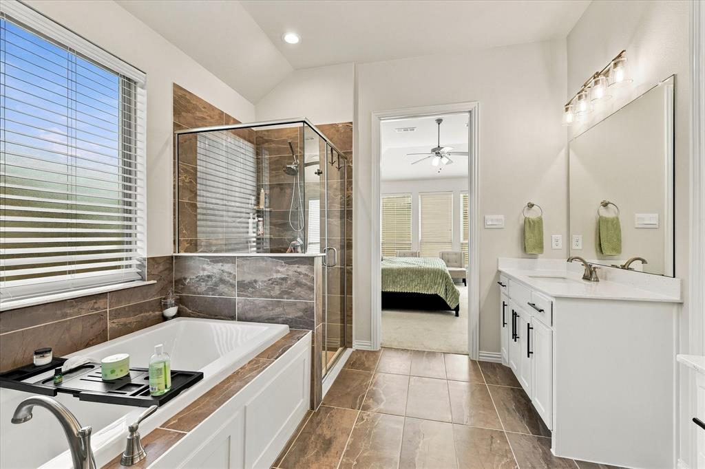 137 Chisos Court Rhome, TX 76078 - Photo 27 of 40 Spacious bathroom featuring a white vanity with under-sink storage, a large mirror, a separate tub, a glass-enclosed shower, and tile flooring