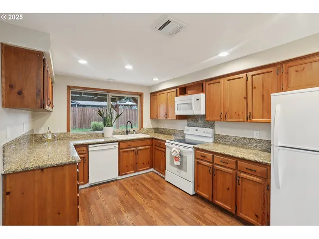 a kitchen with stainless steel appliances granite countertop wooden cabinets a sink a stove a refrigerator and island
