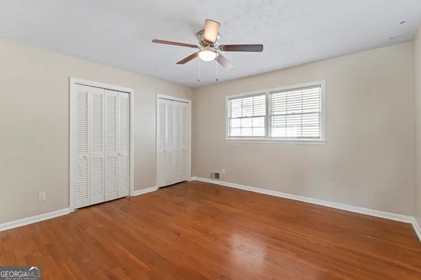 an empty room with wooden floor ceiling fan and windows