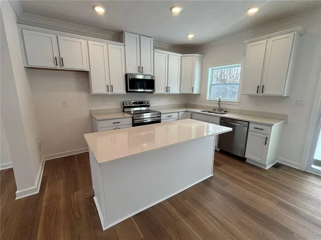 a kitchen with stainless steel appliances a sink a stove a refrigerator cabinets and a wooden floor