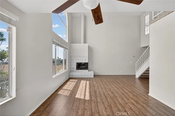 a view of an empty room with wooden floor a ceiling fan and a fireplace