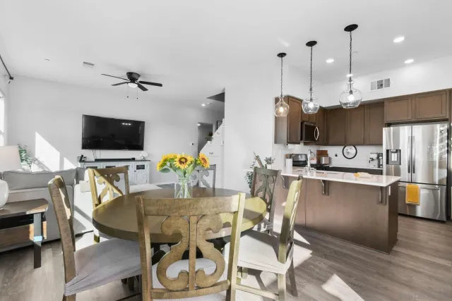 a kitchen with stainless steel appliances kitchen island granite countertop a sink a stove a dining table and chairs with wooden floor